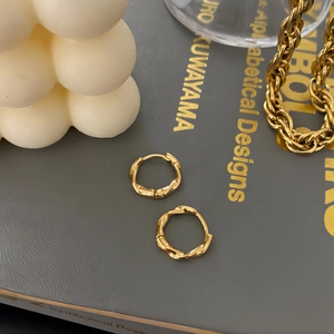 Minimalist 18K gold-plated stainless steel Mobius twist hoop earrings on a decorative book