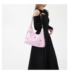 Detailed shot of pink nylon shoulder bag with silver bow charms worn by a model