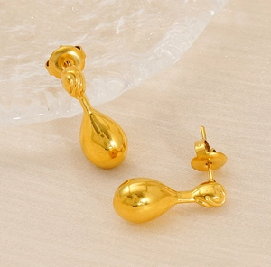 Detail view of gold teardrop earrings on beige fabric with textured glass backdrop