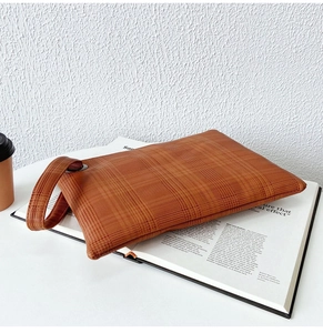 Dettaglio della pochette marrone a scacchi con cinturino su una rivista di moda