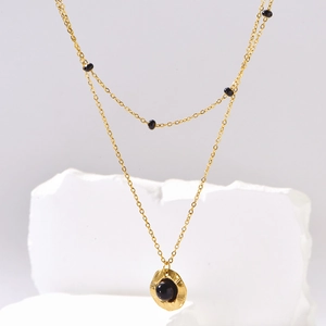 Double-layered gold necklace with irregular pendant and black beads on minimalist white stand