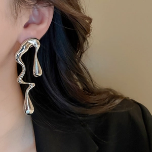 Macro shot of silver liquid metal earrings with irregular dripping design worn on ear