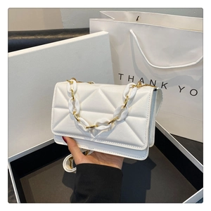 Close-up of white quilted leather flap bag with chunky gold and white chain detail