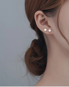 Close-up of minimalist white round pearl earrings worn on ear for an elegant style