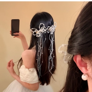 Detailed view of pearl butterfly bow hair clips with long tassels on model's hair.