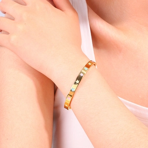 Detailed close-up of a gold titanium bangle with colorful enamel star charms on a model