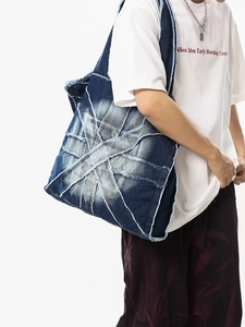 Large blue denim tote bag with patch design and fringe detail shown on a model