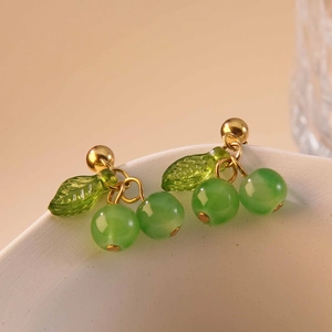 Close-up of sweet green cherry earrings with gold leaf details on a ceramic bowl