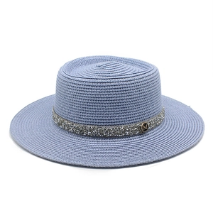 Detail of light blue straw boater hat featuring a crystal band and golden M logo