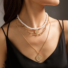 Close-up of layered necklace featuring gold coin pendants and white faux pearls