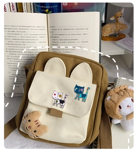 Detail of canvas crossbody bag with rabbit ears, cat patch embroidery and plush pendant