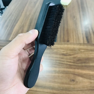 Macro shot of a man's hand holding a curved black wooden beard brush with dense bristles