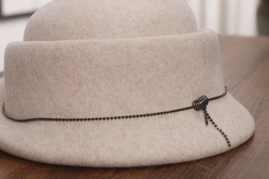 Detail of beige wool felt hat featuring a fine black metal chain and tassel decoration
