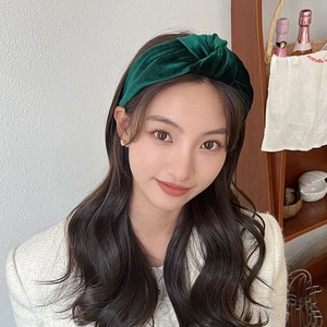 Detail view of a dark green velvet knotted headband worn by a model in a cozy setting