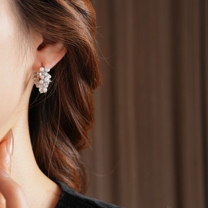 Detail of elegant U-shaped pearl and zircon earrings worn by a model in soft lighting