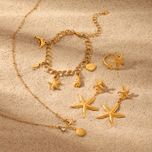 Golden starfish and shell jewelry set including necklace, bracelet and ring on a sandy beach