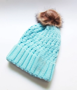 Close-up of light blue cable knit beanie with ribbed cuff and brown faux fur pom-pom