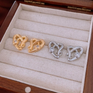 Macro detail of gold and silver snake-shaped heart earrings with sparkling cubic zirconia