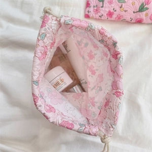 Pink floral drawstring bag showing inner capacity with various skincare cosmetics