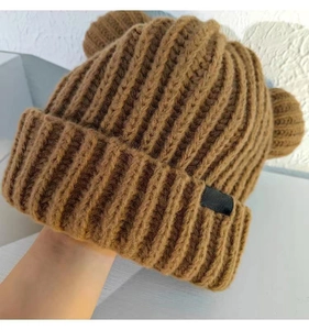 Détail du bonnet en grosse maille marron avec pompons en oreilles d'ours sur le dessus