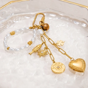 Golden DIY beaded charm chain with heart, sun and pearl pendants in a glass tray