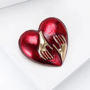 Fashionable red enamel heart brooch with golden metal hugging hands detail on white background