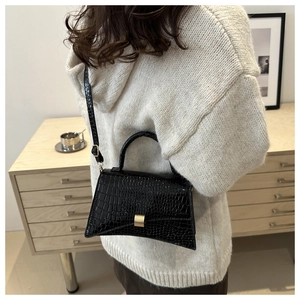 Detail of black crocodile pattern bag with gold clasp shown on model in cozy home setting