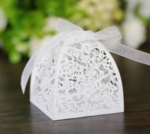 Detailed laser-cut floral pattern on a white paper wedding favor box with organza ribbon
