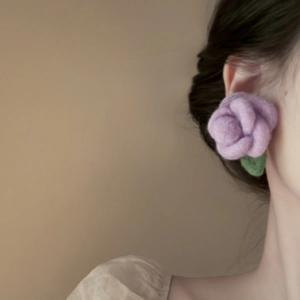 Close-up of wool felt purple rose flower earring with green leaves worn on model ear