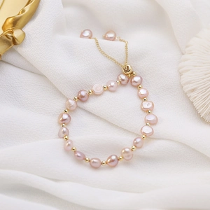 Detailed macro of irregular purple freshwater pearls with gold beads on white silk