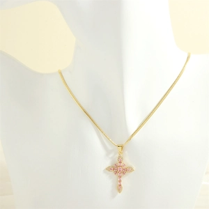 Detail of pink zirconia cross pendant on gold snake chain worn on a white mannequin