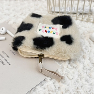 Detail of plush cow print mini pouch with zipper closure on a soft white background