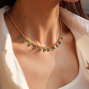 Detail view of gold necklace with green teardrop crystal charms on a female model