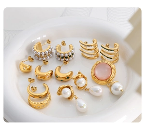 Detailed close-up of C-shaped gold earrings with pearls and zircons in a ceramic tray