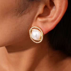 Detail of elegant gold earring featuring a large white pearl surrounded by double-row rhinestones