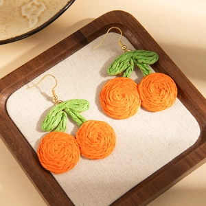 Detailed shot of handmade woven orange fruit earrings on a rustic wooden jewelry tray