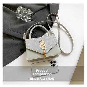 Detail of grey crossbody bag featuring a golden S logo and elegant tassel accents