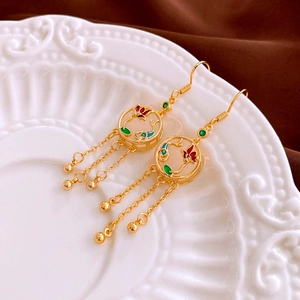 Détail de boucles d'oreilles dorées à pompons avec carpe en zircon et émail sur assiette