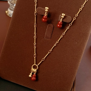 Detail of 18k gold plated necklace and earrings set with red gourd pendants on brown velvet