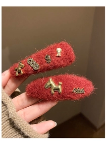 Close-up of red plush hair clips featuring golden horse and metal charms detail