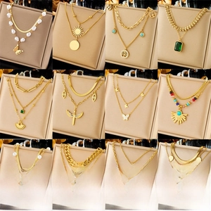 Collection of layered gold necklaces with butterfly, tree of life and emerald pendants