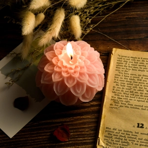 Pink lotus flower shaped scented candle with layered petals lit on vintage wood table