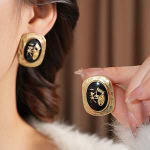 Detail of vintage oval gold earrings with black enamel and embossed carriage design
