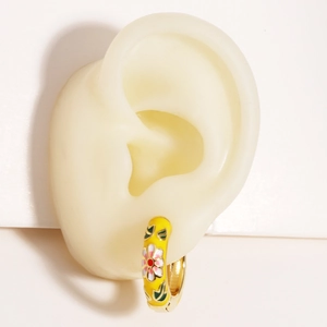 Détail de boucles d'oreilles créoles fleurs en émail jaune portées sur un mannequin pro