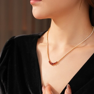 Close-up of elegant gold necklace featuring a curve of sparkling red gemstones on a model