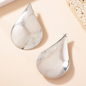 Detailed macro view of large silver teardrop earrings with a brushed metallic texture