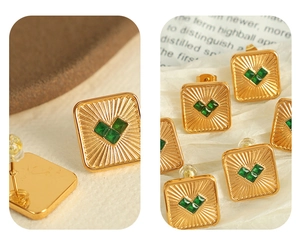Macro detail of gold square stud earrings with green heart stones and radiating texture