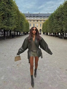 Dark green leather jacket styled with olive shorts and black boots in a park setting