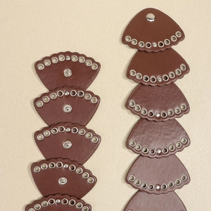 Dettaglio dei componenti della cintura in pelle marrone a ventaglio con occhielli metallici