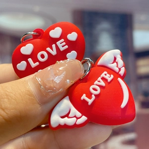 Cute red heart PVC keychains with LOVE text and wings held in hand for couples